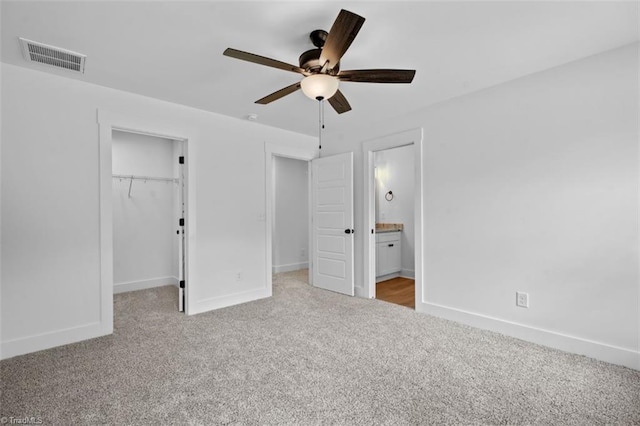 unfurnished bedroom with light carpet, ensuite bathroom, ceiling fan, a closet, and a walk in closet