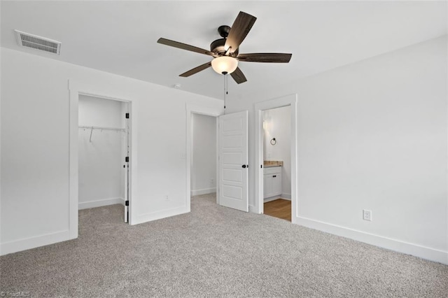 unfurnished bedroom featuring ceiling fan, ensuite bath, light carpet, and a spacious closet