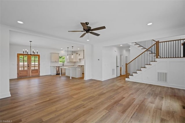 unfurnished living room featuring ceiling fan with notable chandelier, light hardwood / wood-style flooring, and ornamental molding