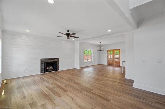 unfurnished living room with a fireplace, ceiling fan with notable chandelier, and light hardwood / wood-style flooring