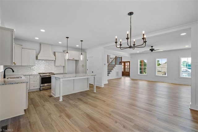 kitchen featuring a center island, sink, stainless steel gas stove, decorative light fixtures, and premium range hood