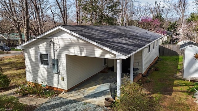 exterior space featuring a carport, fence, a shingled roof, and driveway