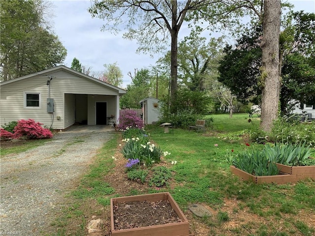 view of yard with an outbuilding, a vegetable garden, a storage shed, a carport, and gravel driveway
