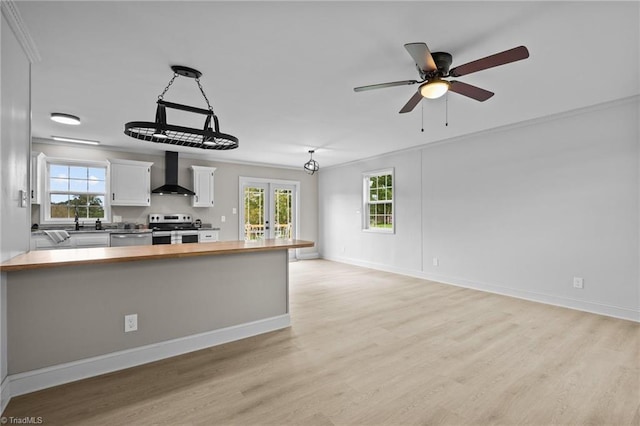 kitchen featuring wall chimney range hood, white cabinets, plenty of natural light, wooden counters, and stainless steel appliances