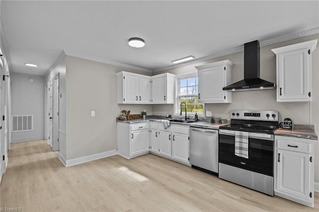 kitchen featuring appliances with stainless steel finishes, light hardwood / wood-style floors, wall chimney exhaust hood, white cabinets, and crown molding