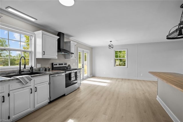 kitchen with wall chimney exhaust hood, appliances with stainless steel finishes, white cabinets, and decorative light fixtures