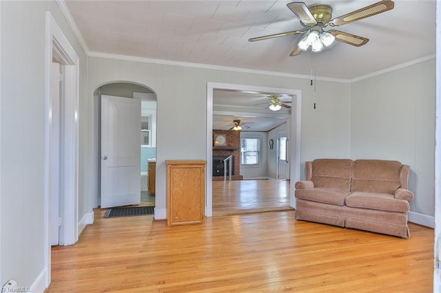 living area with light wood-style flooring, a fireplace, arched walkways, and crown molding