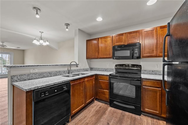 kitchen with sink, kitchen peninsula, light stone countertops, hardwood / wood-style floors, and black appliances