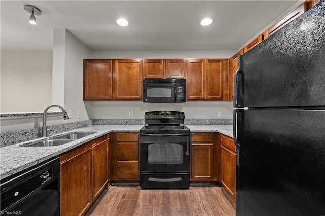 kitchen with light stone counters, wood-type flooring, sink, and black appliances