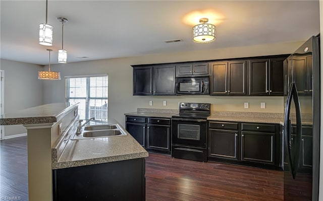 kitchen featuring pendant lighting, a kitchen island with sink, black appliances, sink, and dark hardwood / wood-style floors