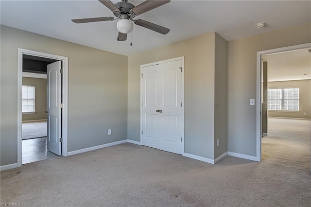 unfurnished bedroom with light colored carpet, multiple windows, and ceiling fan