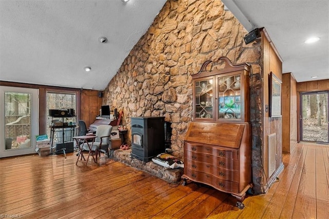 living area featuring a wood stove, vaulted ceiling, wood-type flooring, and a textured ceiling