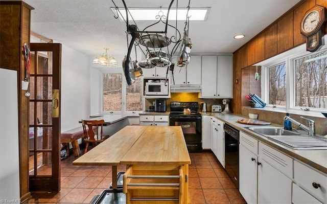 kitchen with black appliances, dark tile patterned floors, under cabinet range hood, and a sink