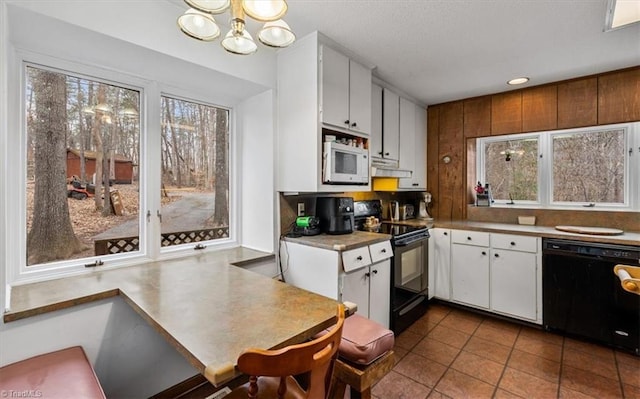 kitchen with a chandelier, tile patterned floors, light countertops, black appliances, and white cabinetry