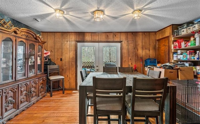 dining room with a textured ceiling, french doors, light wood-type flooring, and wooden walls