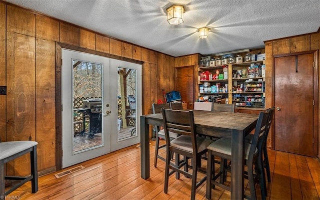 dining area with wood walls, visible vents, light wood finished floors, and french doors