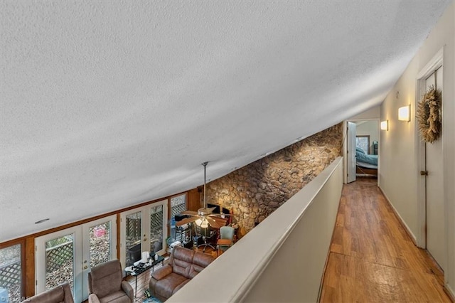 hall featuring light wood-type flooring, vaulted ceiling, a textured ceiling, and french doors