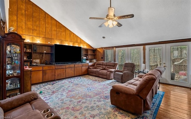 living area with built in shelves, lofted ceiling, wood-type flooring, wood walls, and ceiling fan