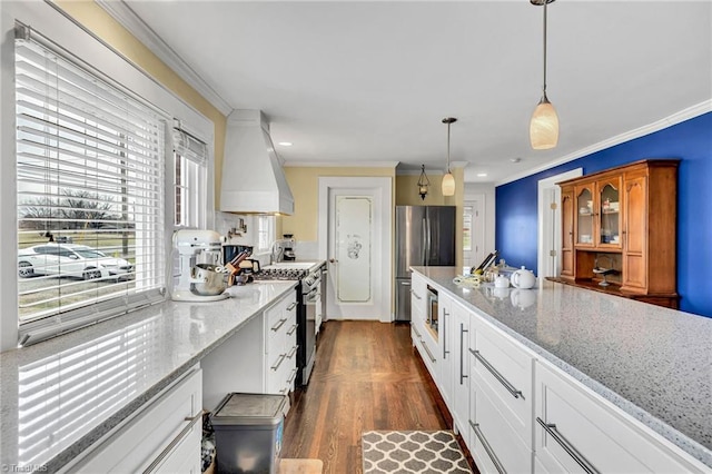 kitchen featuring pendant lighting, appliances with stainless steel finishes, white cabinetry, premium range hood, and light stone counters