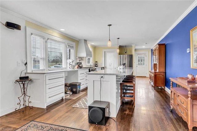 kitchen featuring pendant lighting, stainless steel refrigerator, white cabinets, a kitchen bar, and a center island