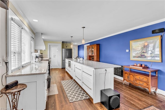 kitchen featuring appliances with stainless steel finishes, decorative light fixtures, white cabinets, a center island, and custom range hood