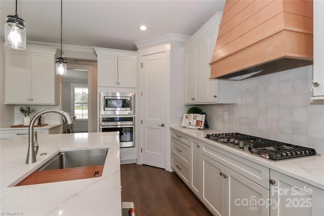 kitchen featuring stainless steel appliances, white cabinetry, a sink, custom range hood, and pendant lighting