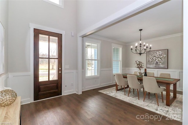 foyer with a wainscoted wall, a notable chandelier, ornamental molding, and wood-type flooring