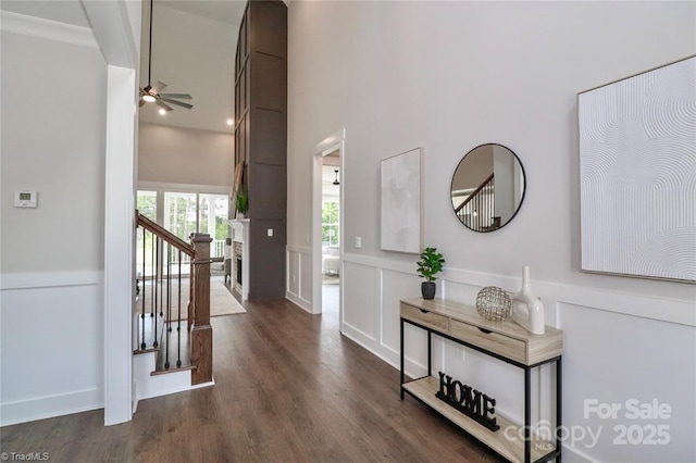 hallway with a wainscoted wall, stairway, dark wood finished floors, a decorative wall, and a towering ceiling