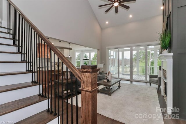 staircase with high vaulted ceiling, a fireplace, wood finished floors, recessed lighting, and a ceiling fan