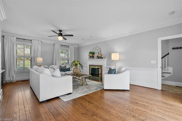 living room with a brick fireplace, stairs, ornamental molding, hardwood / wood-style floors, and a ceiling fan