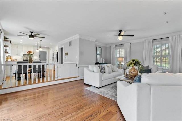 living room with light wood finished floors, visible vents, ceiling fan, and ornamental molding