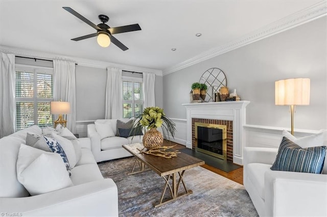 living room with wood finished floors, baseboards, ceiling fan, ornamental molding, and a brick fireplace