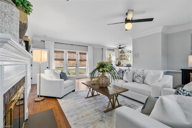 living area with a fireplace, crown molding, wood finished floors, and ceiling fan