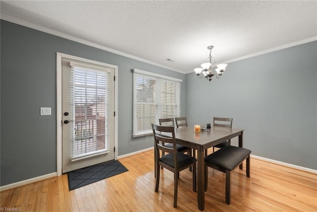 dining area featuring a textured ceiling, light wood-type flooring, ornamental molding, and a chandelier