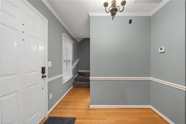 foyer entrance featuring hardwood / wood-style floors, ornamental molding, and an inviting chandelier