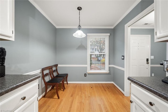 kitchen with white cabinets, light hardwood / wood-style floors, hanging light fixtures, and crown molding