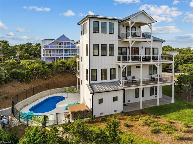 rear view of property featuring a balcony, a patio area, and a fenced in pool