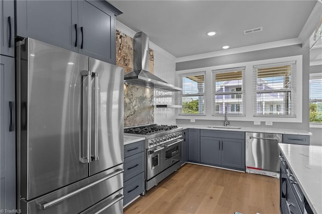 kitchen with premium appliances, sink, light wood-type flooring, wall chimney exhaust hood, and gray cabinets