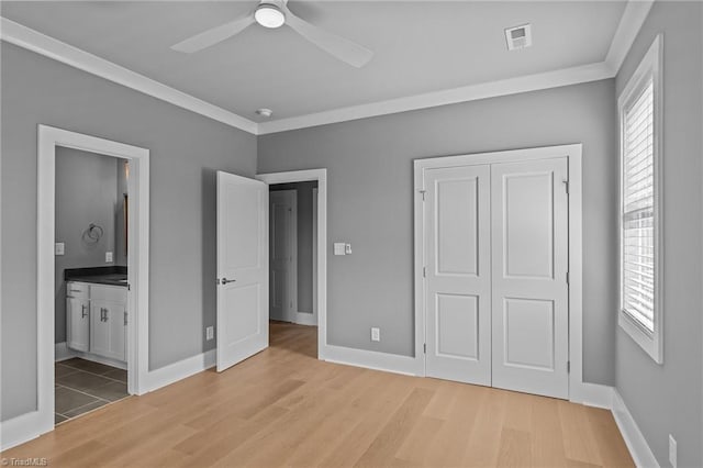 unfurnished bedroom featuring ceiling fan, light wood-type flooring, ornamental molding, a closet, and ensuite bath