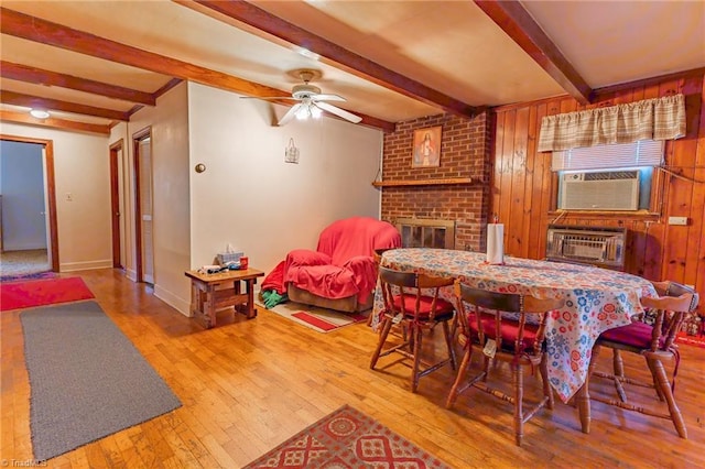 dining area featuring hardwood / wood-style flooring, wooden walls, cooling unit, a brick fireplace, and ceiling fan