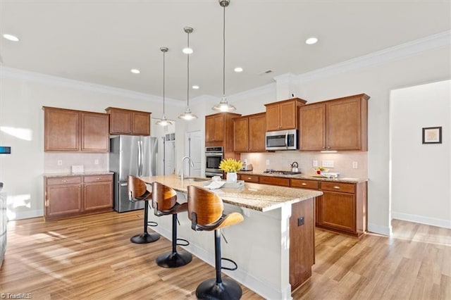 kitchen with hanging light fixtures, appliances with stainless steel finishes, a kitchen island with sink, and a breakfast bar area