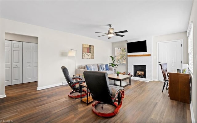 living room with ceiling fan, wood-type flooring, and a brick fireplace