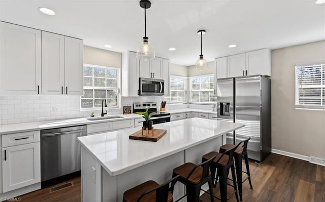 kitchen featuring sink, decorative light fixtures, a center island, appliances with stainless steel finishes, and white cabinets