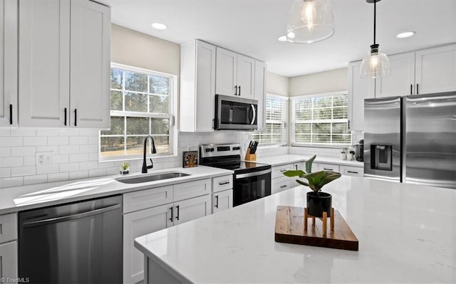 kitchen with sink, appliances with stainless steel finishes, backsplash, white cabinets, and decorative light fixtures