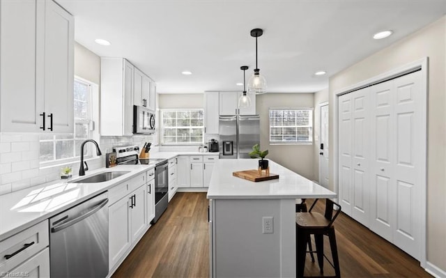 kitchen featuring sink, white cabinetry, hanging light fixtures, stainless steel appliances, and a center island