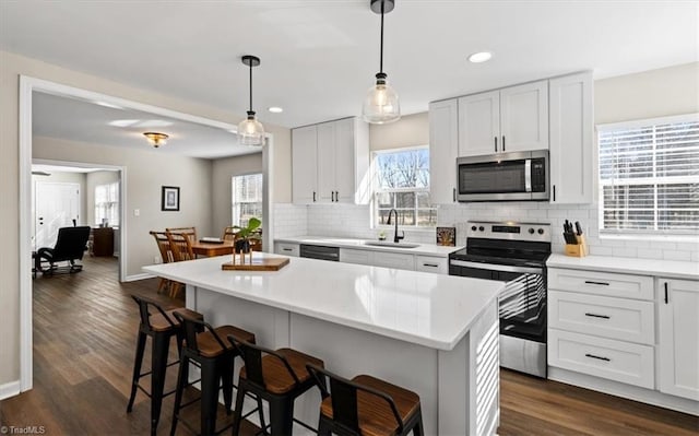 kitchen with sink, white cabinetry, a center island, hanging light fixtures, and appliances with stainless steel finishes