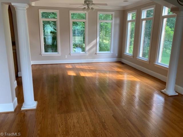 interior space with decorative columns, a wealth of natural light, ceiling fan, and wood-type flooring