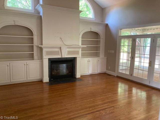 unfurnished living room with built in shelves, dark wood-type flooring, and a high ceiling