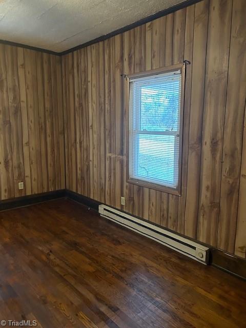 empty room with wood walls, dark hardwood / wood-style flooring, and a baseboard radiator