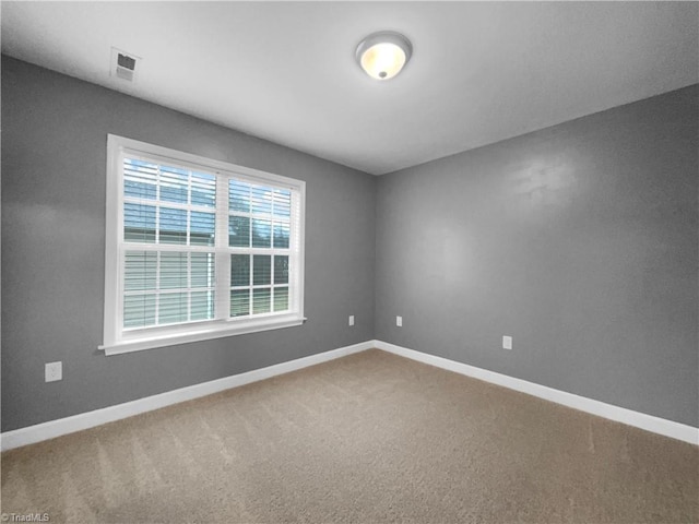 empty room with carpet floors, visible vents, and baseboards